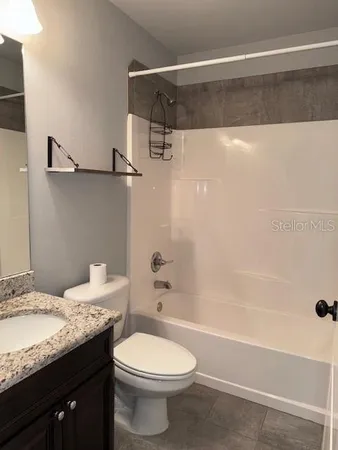 a bathroom with a granite countertop bathtub shower sink vanity and toilet