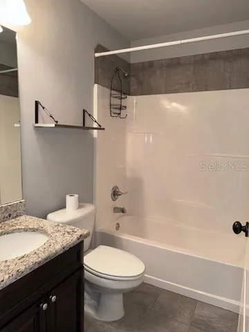 a bathroom with a granite countertop bathtub shower sink vanity and toilet