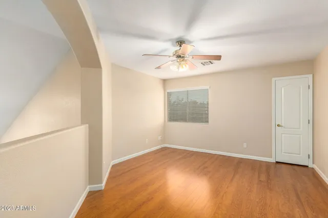 a view of an empty room with chandelier fan and wooden floor