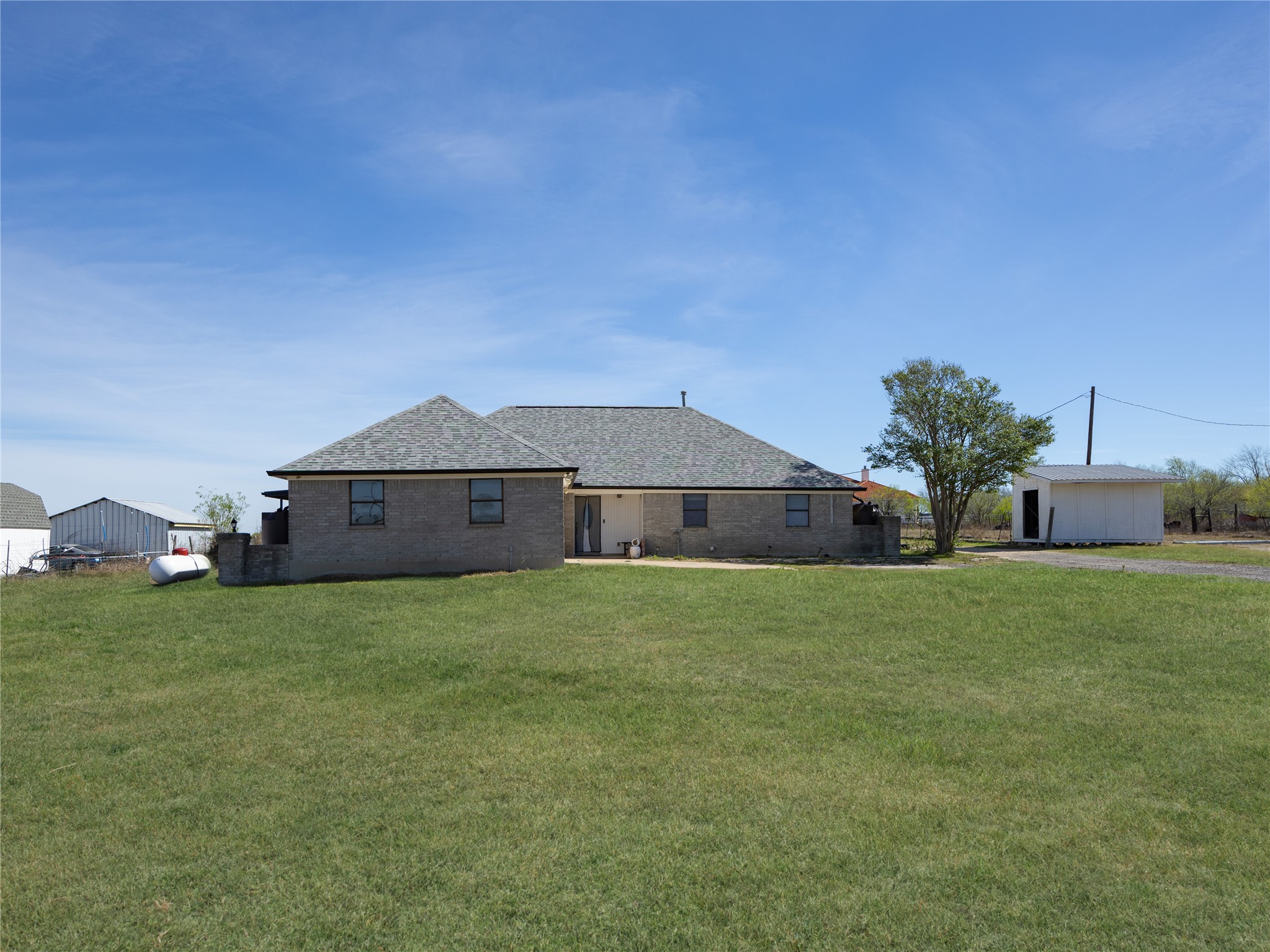 2412 Williamson Road Lockhart, TX 78644 - Photo 17 of 36 Rear exterior featuring a brick facade, shingled roof, a covered patio area, and an expansive lawn