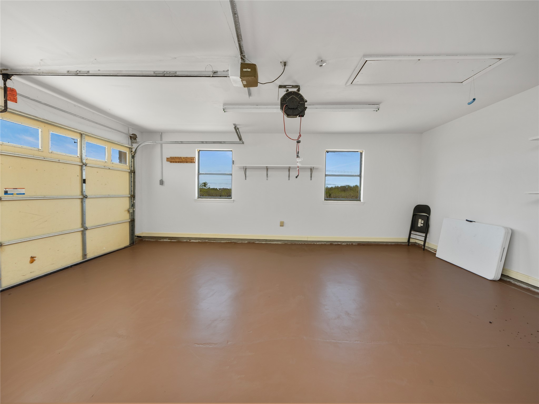 2412 Williamson Road Lockhart, TX 78644 - Photo 18 of 36 Spacious garage featuring a durable floor coating, two windows, two fluorescent light fixtures, an automatic garage door opener, and a garage door with multiple translucent panels
