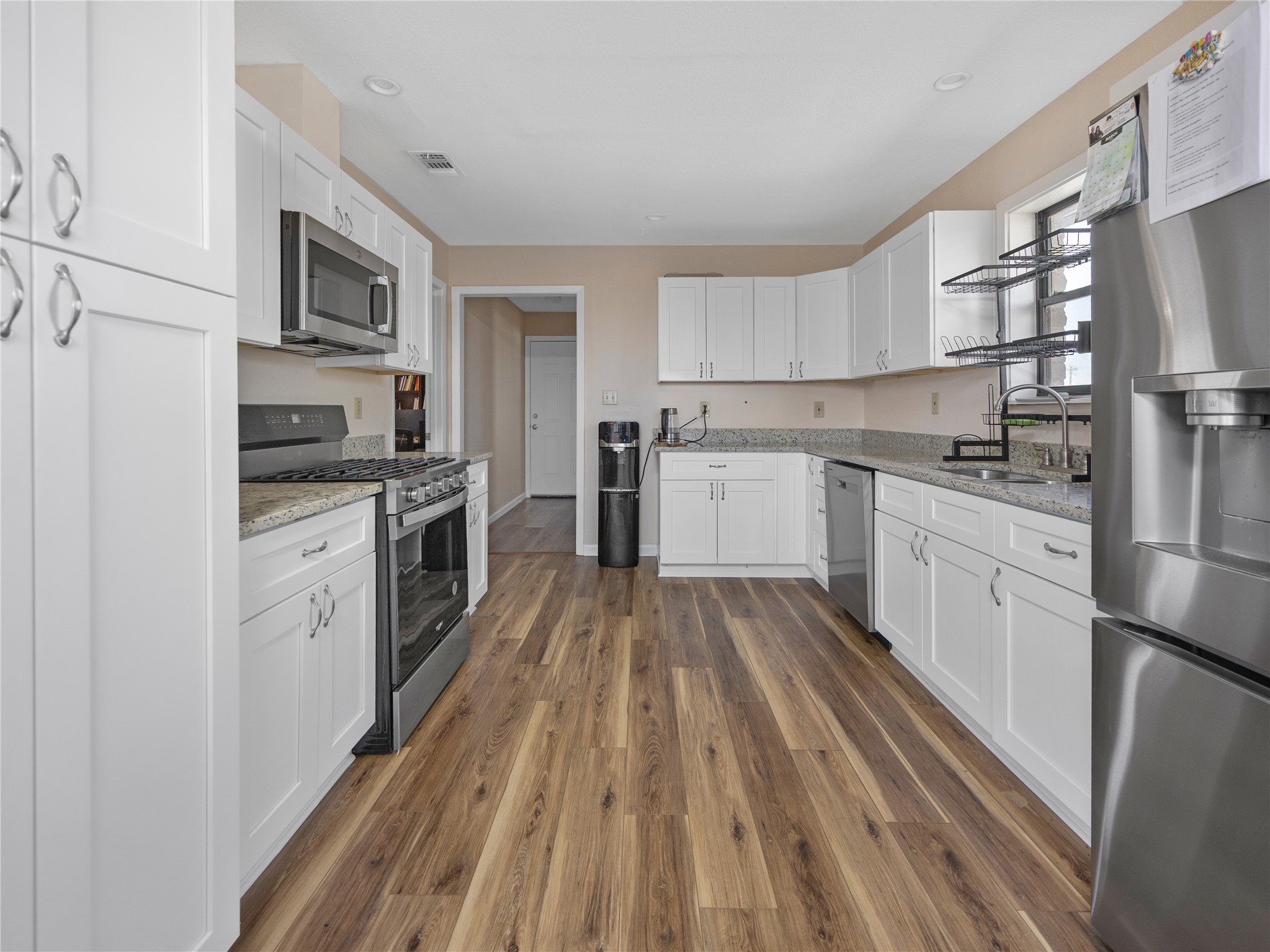 2412 Williamson Road Lockhart, TX 78644 - Photo 19 of 36 Kitchen featuring wood-finish flooring, white shaker-style cabinetry, granite-style countertops, stainless steel appliances, and recessed lighting