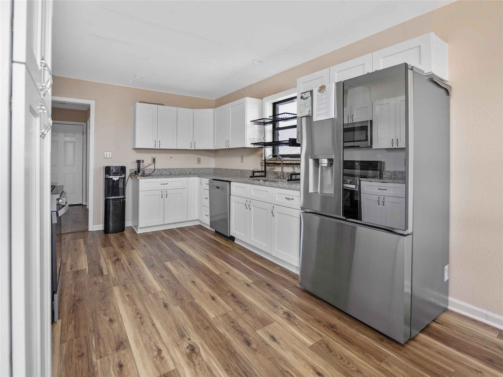 2412 Williamson Road Lockhart, TX 78644 - Photo 25 of 36 Spacious kitchen featuring extensive wood-finish flooring, white cabinetry with silver hardware, granite-look countertops, and stainless steel appliances including a refrigerator and dishwasher