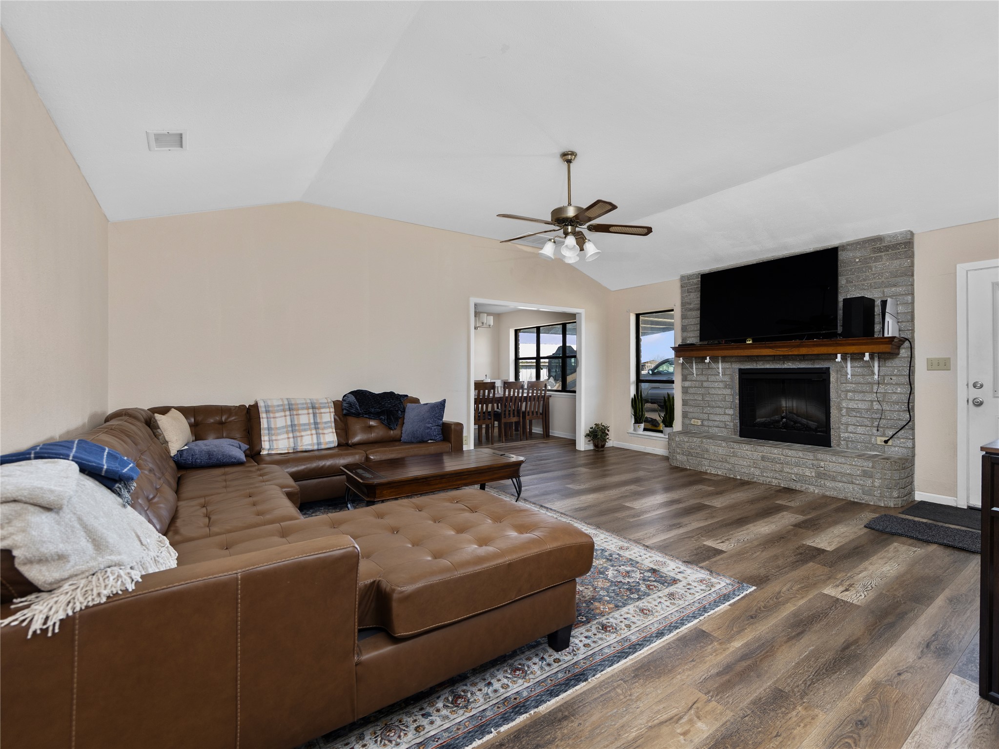 2412 Williamson Road Lockhart, TX 78644 - Photo 3 of 36 Vaulted living area featuring wood-finish flooring, a ceiling fan with integrated lighting, and a stone-clad fireplace with a wood mantel