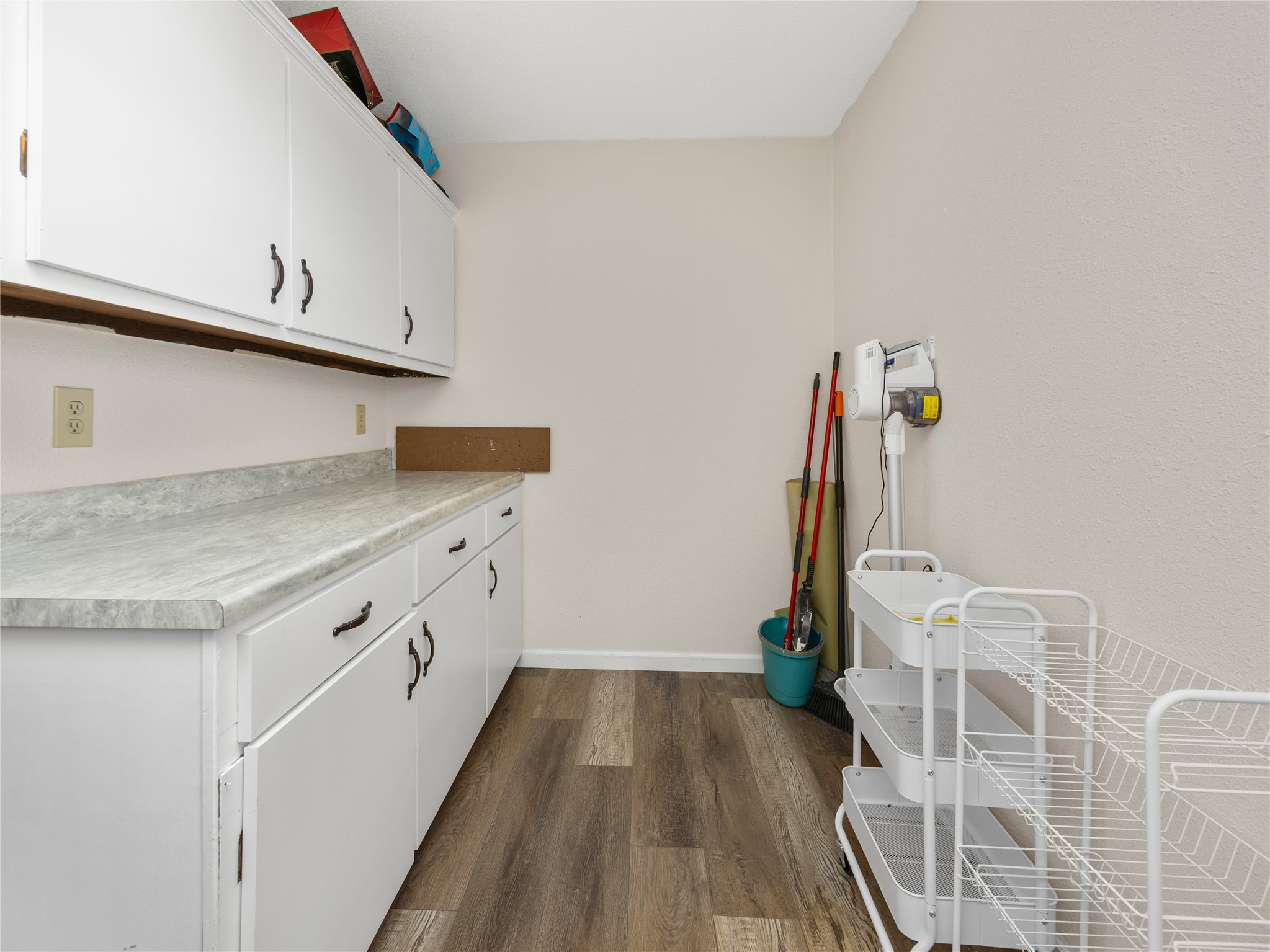2412 Williamson Road Lockhart, TX 78644 - Photo 8 of 36 Utility room featuring white cabinetry with dark hardware, light-toned countertops, and wood-finish flooring