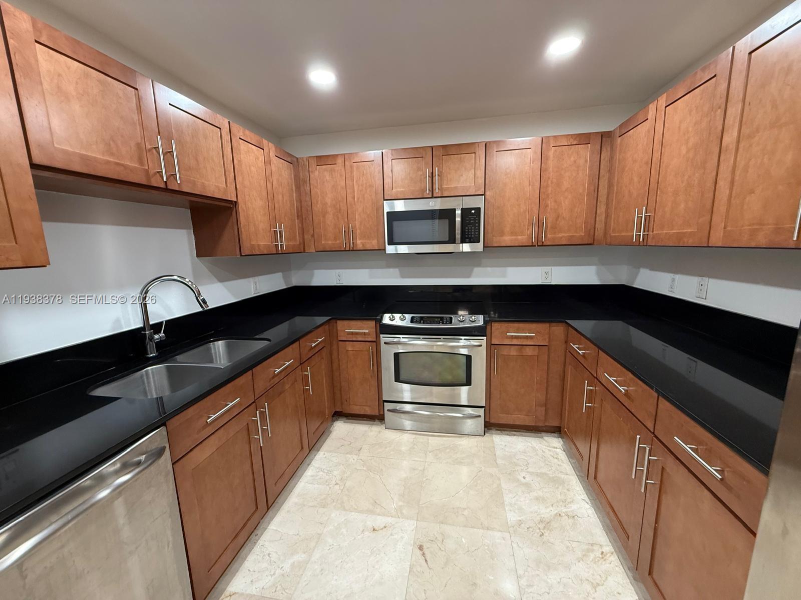 8390 Southwest 72nd Avenue, Unit 520 Miami, FL 33143 - Photo 26 of 61 a kitchen with stainless steel appliances granite countertop a sink a stove top oven and wooden cabinets