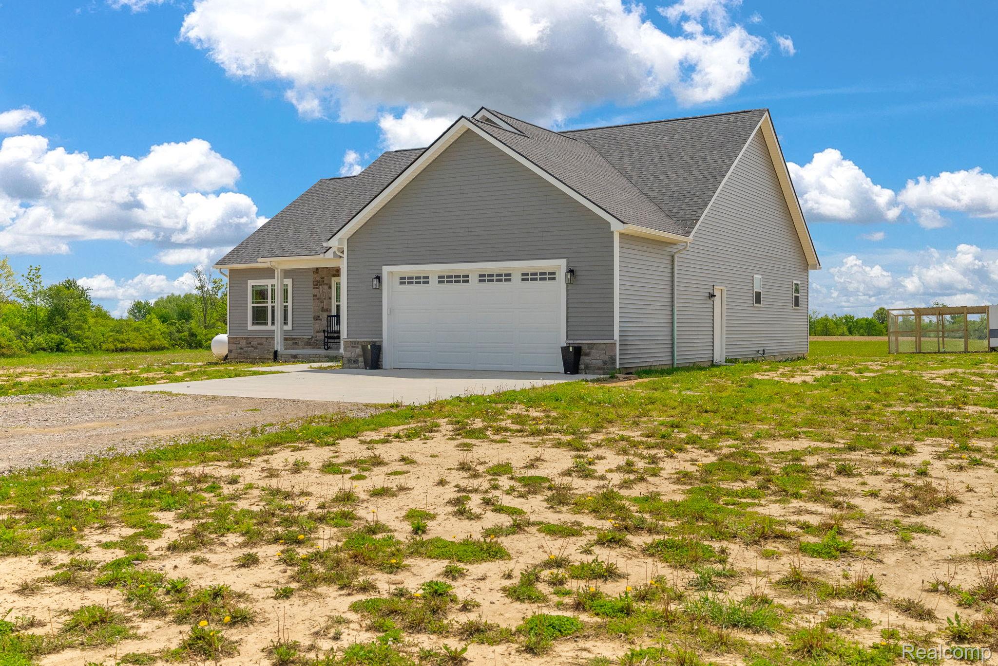 7600 Church Road Imlay City, MI 48444 - Photo 7 of 38 Gray siding residence featuring a two-car garage with a concrete driveway, a covered front entry with stone accents, and a dark shingle roof