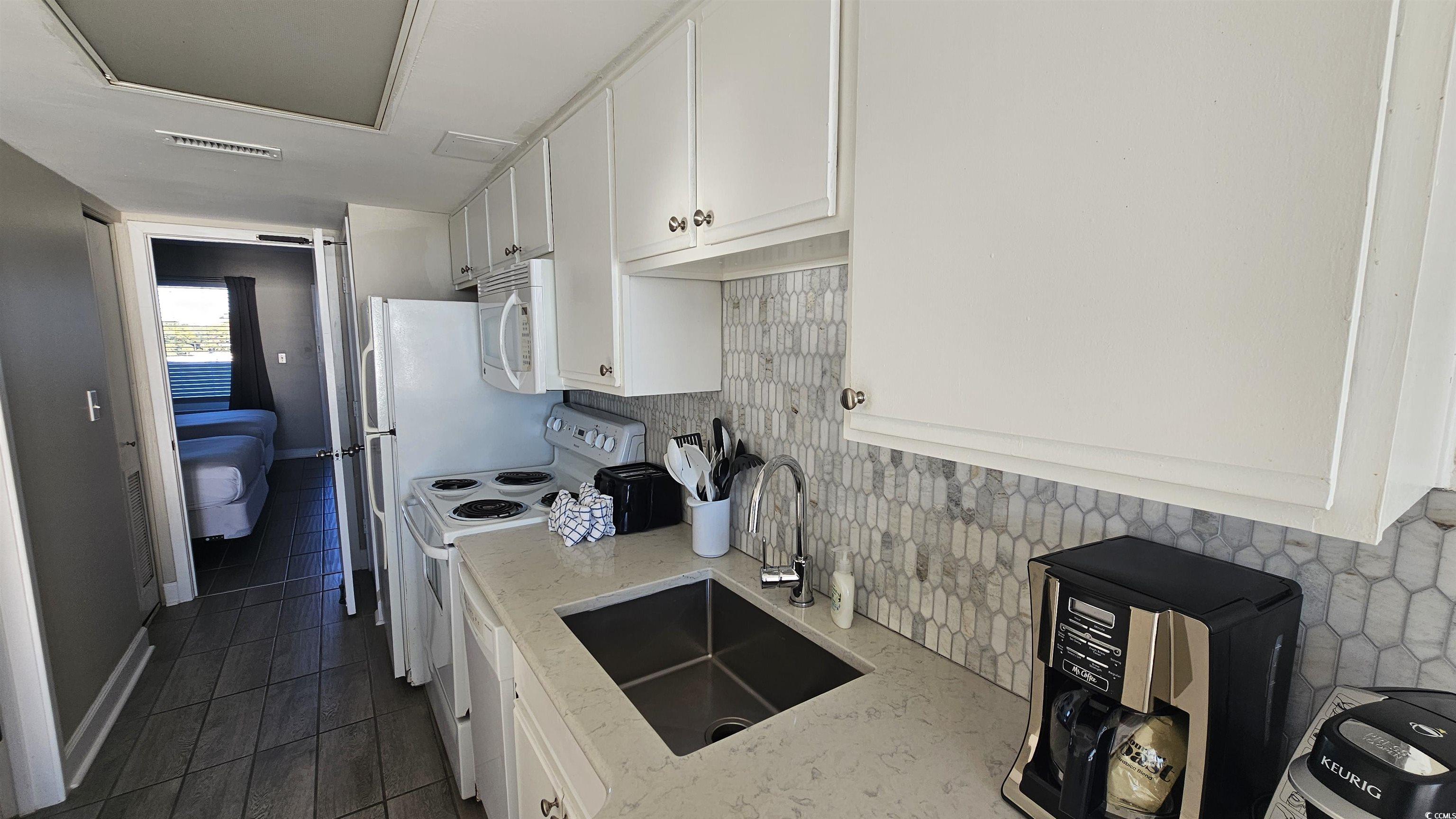 161 Seawatch Drive, Unit 610 Myrtle Beach, SC 29572 - Photo 3 of 35 Kitchen with white cabinets, decorative backsplash, white appliances, and light stone counters