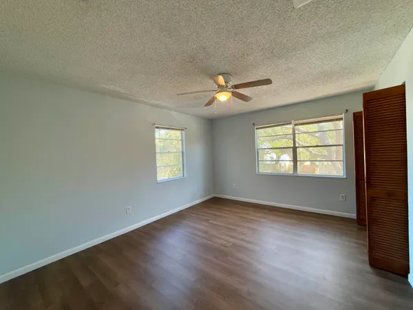 an empty room with wooden floor chandelier fan and windows