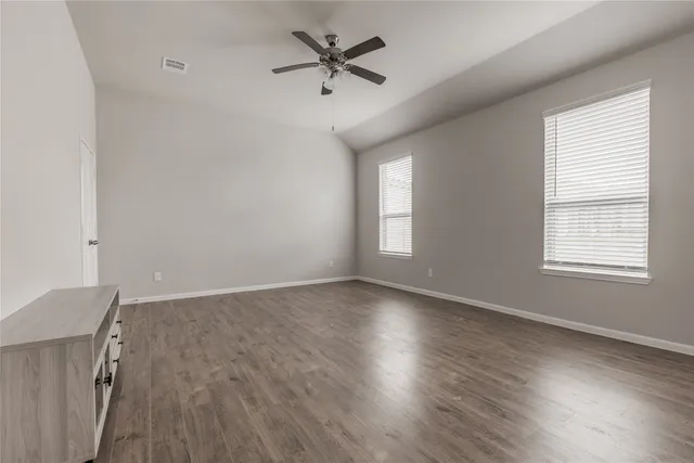 an empty room with wooden floor fan and windows