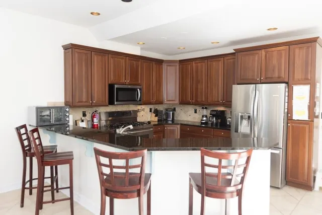 a kitchen with stainless steel appliances granite countertop a refrigerator a stove a dining table and chairs