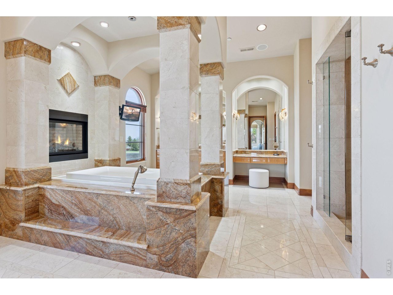 6541 Legend Ridge Trail Niwot, CO 80503 - Photo 26 of 45 Luxurious Primary Bathroom with a central infinity waterfall soaking tub with arched details and colums framing the tub, a gas fireplace with granite surround, fully enclosed steam shower and marble flooring.