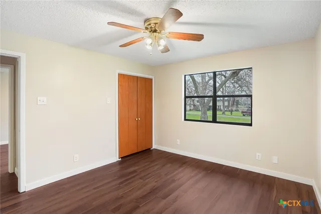 an empty room with wooden floor chandelier fan and windows