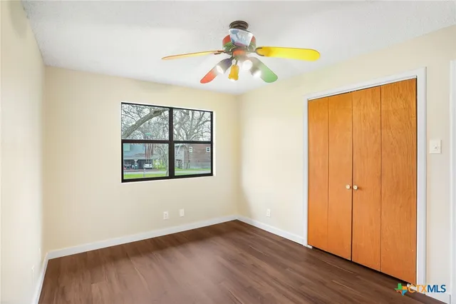 an empty room with wooden floor chandelier fan and windows
