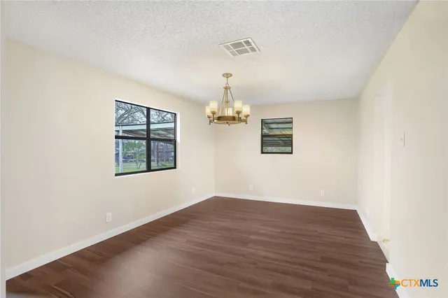 an empty room with wooden floor chandelier and windows