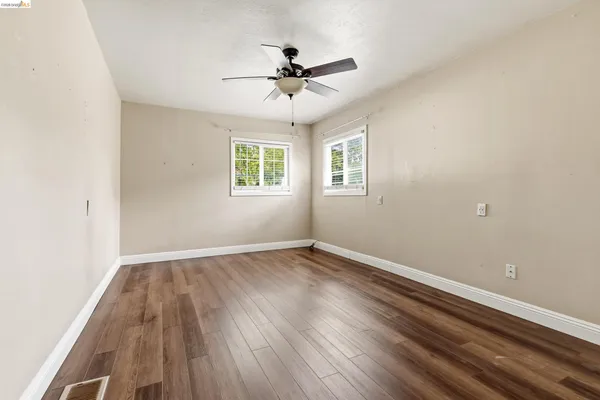 an empty room with wooden floor chandelier fan and windows