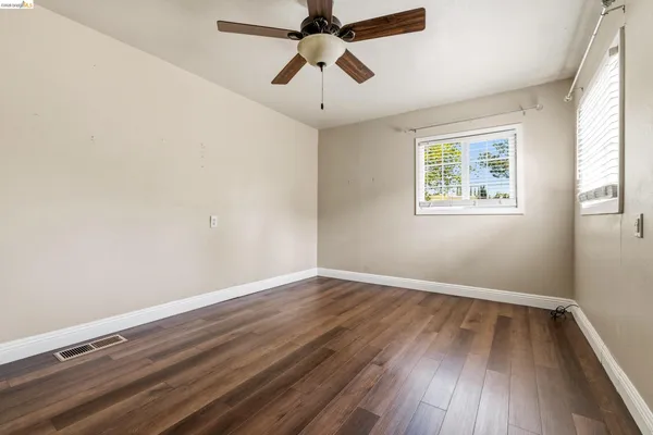 an empty room with wooden floor ceiling fan and windows