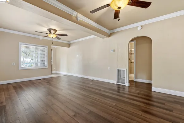 a view of an empty room with wooden floor and a ceiling fan