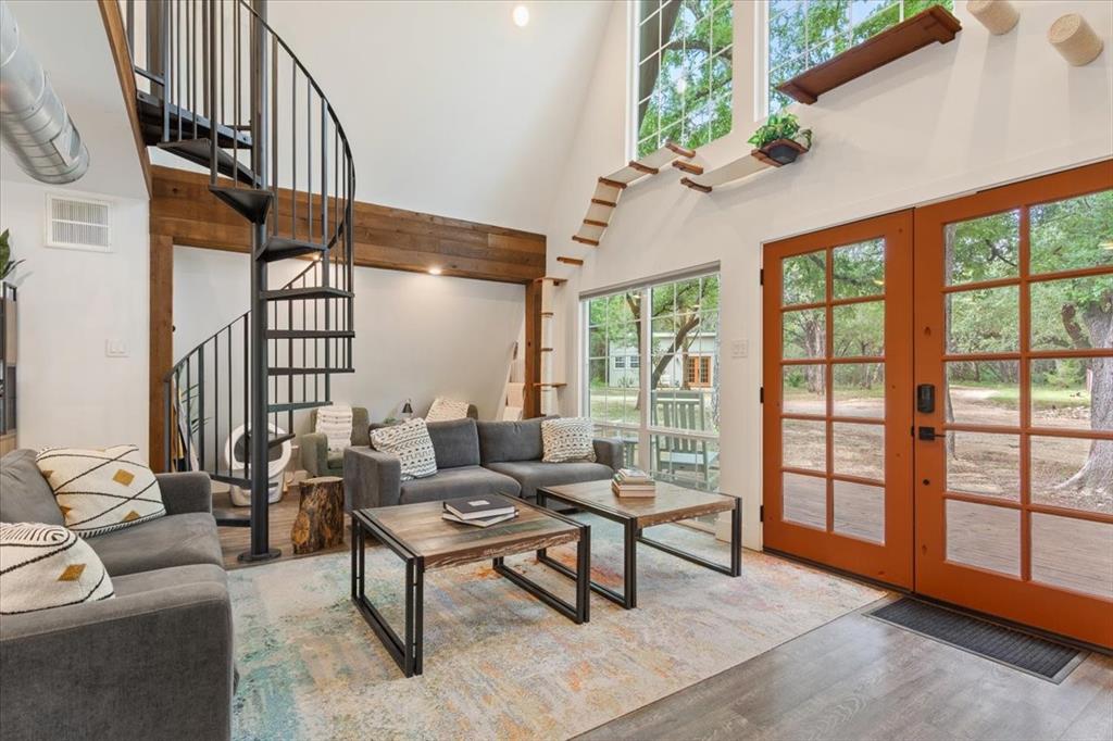 15988 Wortham Bend Road China Spring, TX 76633 - Photo 5 of 40 Vaulted ceiling living area featuring a black metal spiral staircase, wood-finish flooring, exposed wood beams, and a pair of terra cotta-toned double doors with transom windows