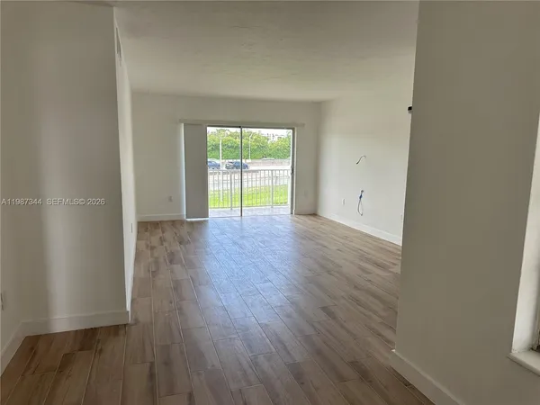 a view of an empty room with wooden floor and a window