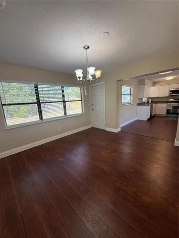 an empty room with wooden floor chandelier and windows