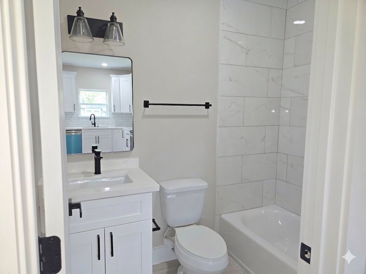 7830 Woodlyn Road, Unit B Houston, TX 77028 - Photo 7 of 10 Modern bathroom with a clean vanity, quartz countertop, black fixtures, and a tiled tub/shower surround