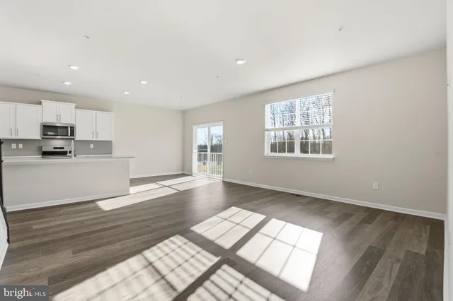a view of an empty room with kitchen and window