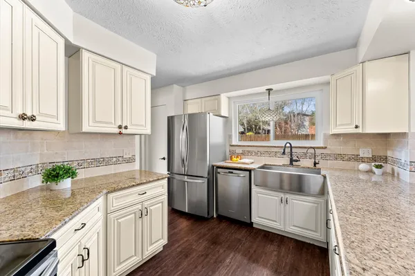 a kitchen with stainless steel appliances granite countertop white cabinets a refrigerator a sink a stove a microwave and wooden floors