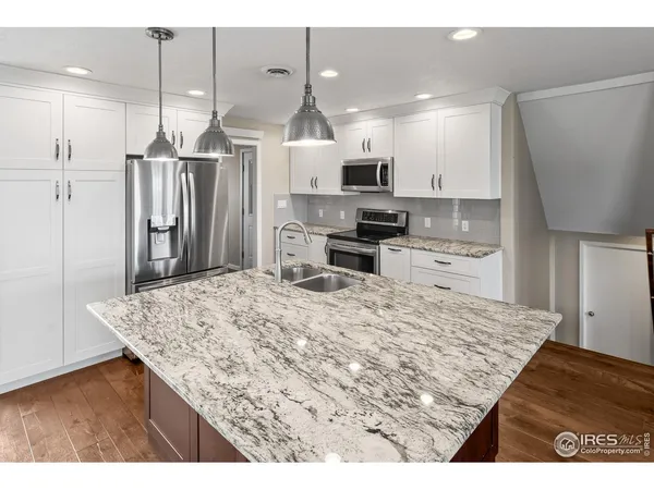 a kitchen with stainless steel appliances granite countertop a refrigerator a sink a stove and a wooden floors