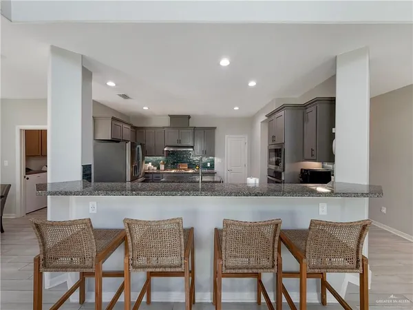 a kitchen with stainless steel appliances granite countertop a dining table chairs refrigerator and microwave