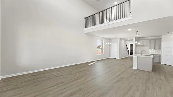 a view of an empty room and kitchen with wooden floor