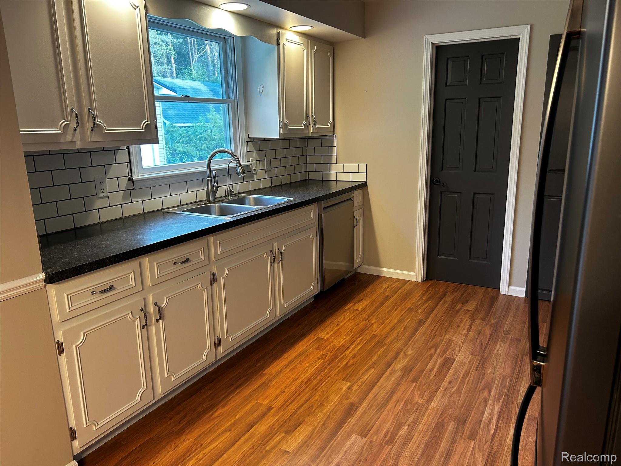 5440 Deland Road Flushing, MI 48433 - Photo 4 of 25 Kitchen featuring wood-finish flooring, light cabinetry with decorative trim, dark countertops, and white subway tile backsplash.