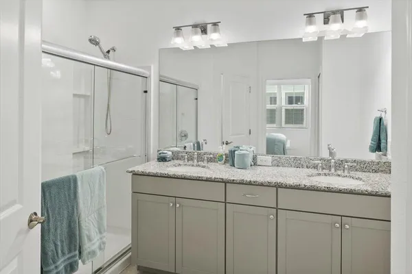 a bathroom with a granite countertop double vanity sink a mirror and a shower