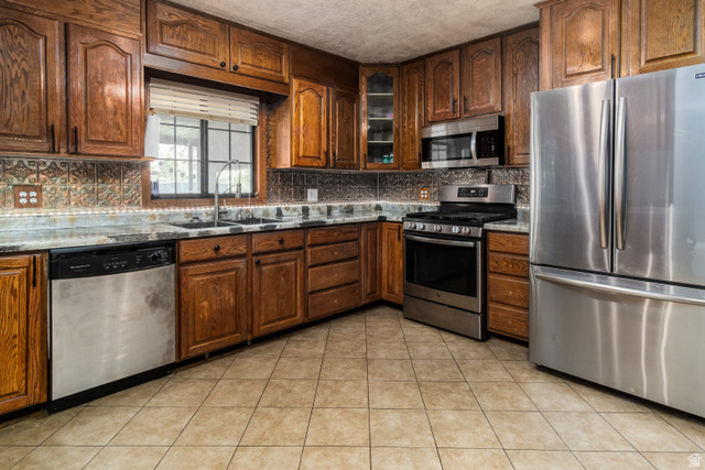 100 Third North Helper, UT 84526 - Photo 17 of 30 Kitchen featuring stainless steel appliances, abundant wood cabinetry, patterned tile backsplash, solid surface countertops, and tile flooring
