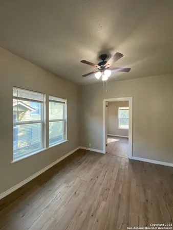 an empty room with wooden floor chandelier fan and windows