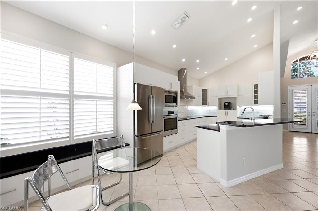 1960 Timarron Way Naples, FL 34109 - Photo 12 of 45 Modern kitchen featuring white cabinetry, stainless steel appliances, and a central island with a sink and dark countertop