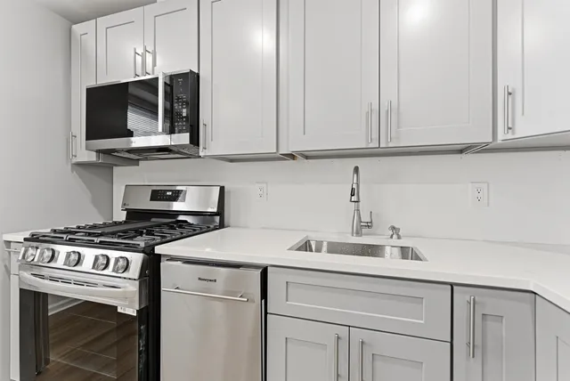 a kitchen with stainless steel appliances granite countertop grey cabinets a stove a sink and dishwasher