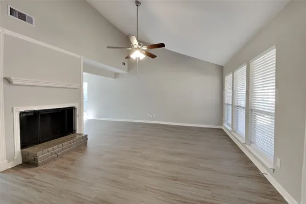 a view of an empty room with wooden floor fireplace and a window