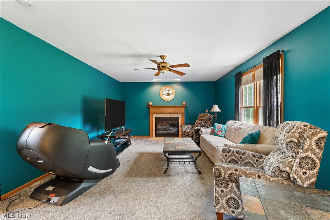 Inviting living space featuring a fireplace with a wood mantle, carpeted flooring, and a ceiling fan with integrated lighting