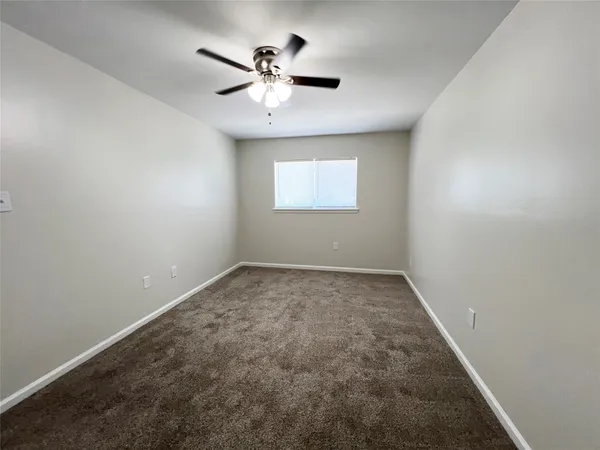 an empty room with a chandelier fan and windows
