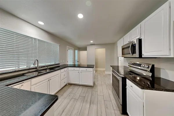 a kitchen with stainless steel appliances granite countertop a sink a stove top oven a chimney wooden floor and cabinets
