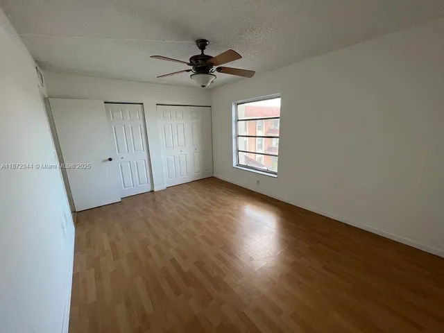 an empty room with wooden floor fan and windows