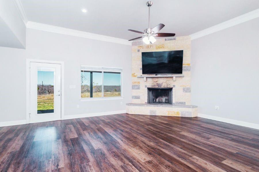 4319 County Road 337 Early, TX 76802 - Photo 5 of 31 Living room featuring crown molding, a stone fireplace, dark wood-style flooring, and ceiling fan