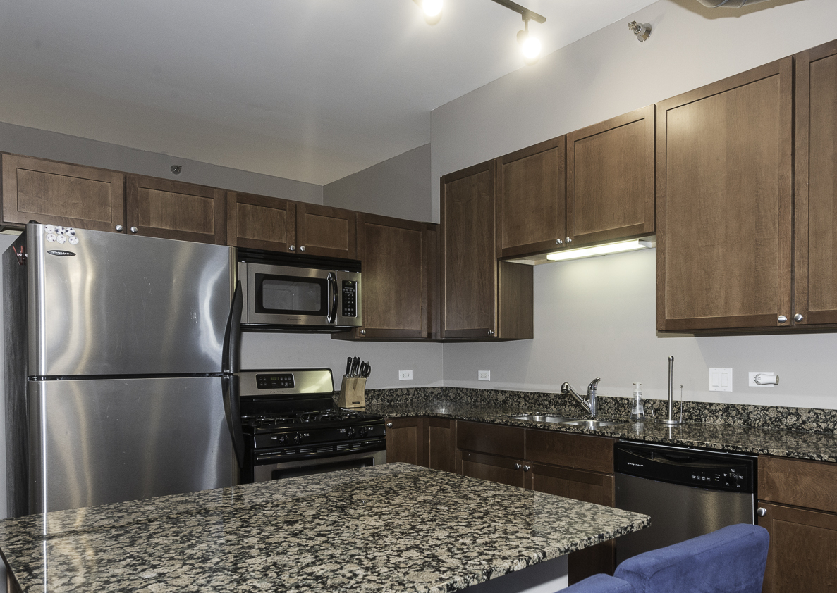 901 West Madison Street, Unit 818 Chicago, IL 60607 - Photo 11 of 26 a kitchen with granite countertop wooden cabinets a refrigerator and a sink