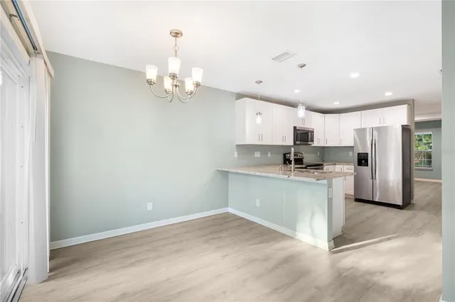 a kitchen with stainless steel appliances granite countertop a refrigerator a sink dishwasher a stove and white cabinets with wooden floor