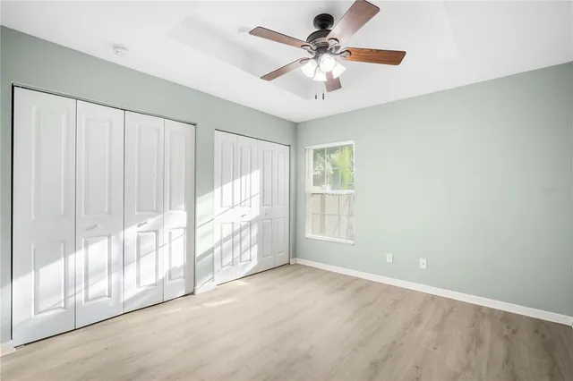 an empty room with wooden floor fan and windows