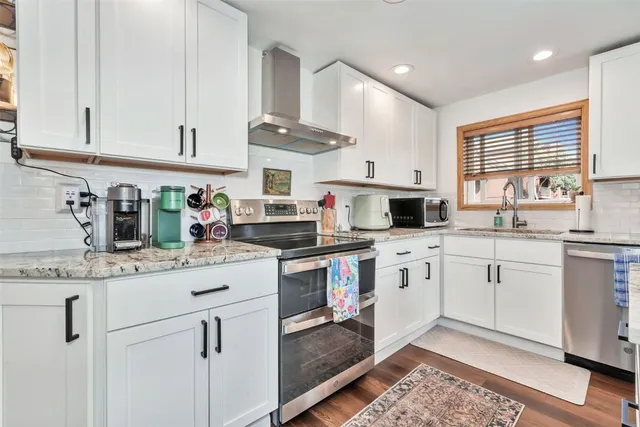 a kitchen with granite countertop white cabinets white appliances a sink and a window