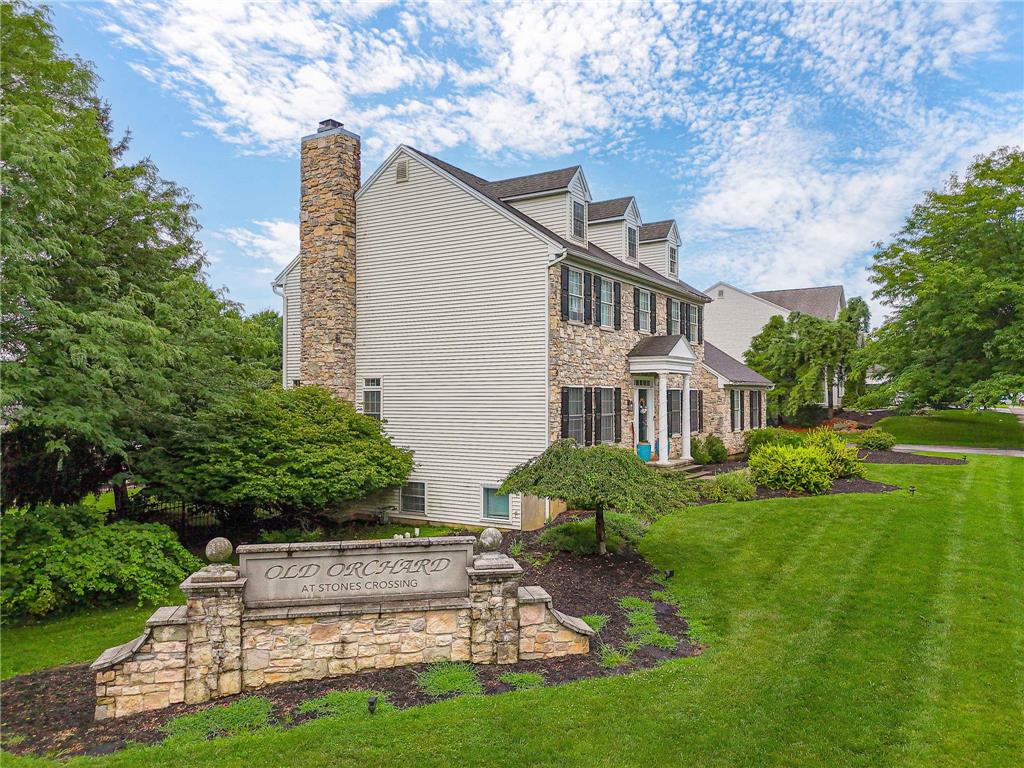 A stone-and-siding exterior rises above a manicured lawn framed by mature trees.
