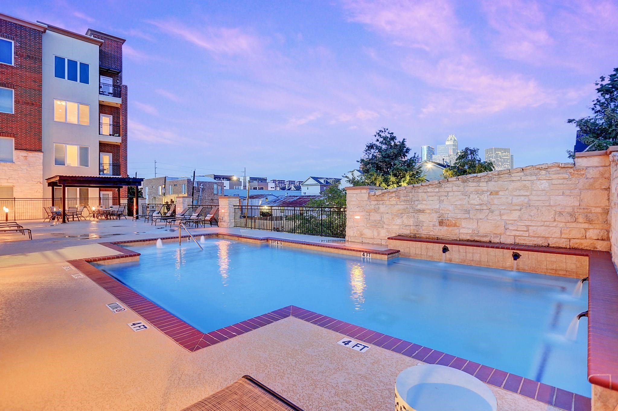 1900 Genesee Street, Unit 203 Houston, TX 77006 - Photo 25 of 30 This photo showcases a modern condo complex with a well-lit outdoor pool area, featuring a stone wall and city views in the background, perfect for relaxation and entertaining.