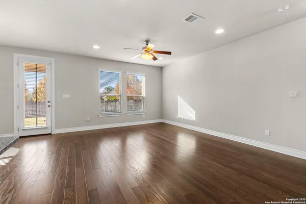 an empty room with wooden floor fan and windows